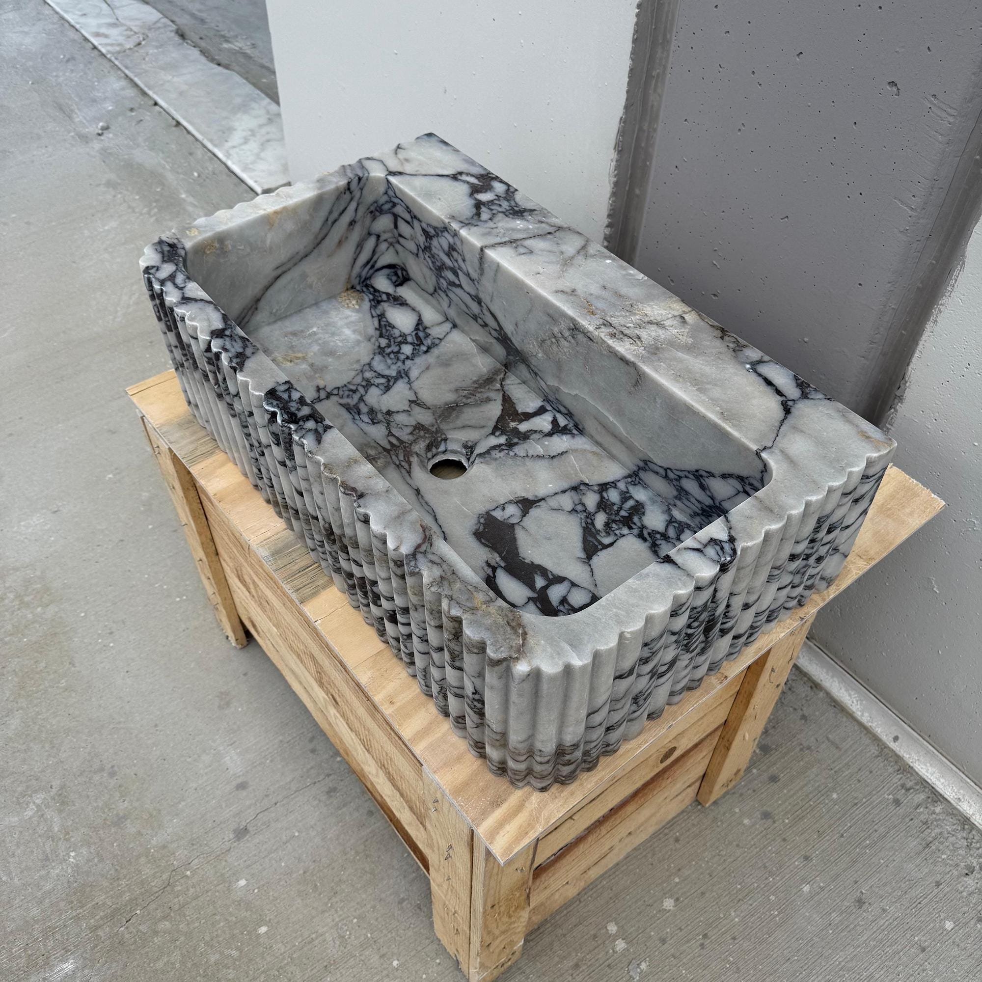 A luxury bathroom vessel sink carved from premium Italian marble is displayed outdoors.