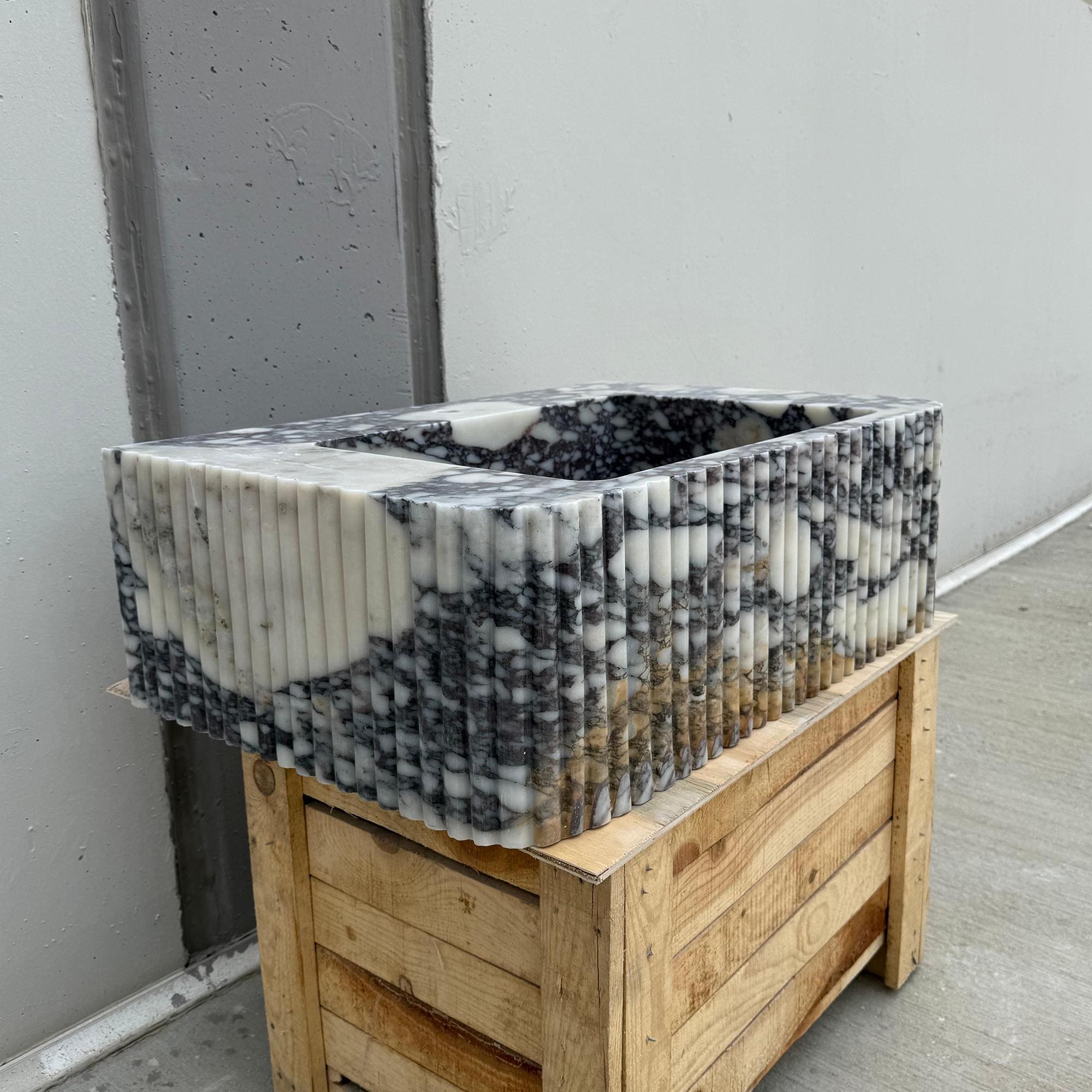 Calacatta Viola marble sink on crate, showcasing artisan-crafted ribbed design