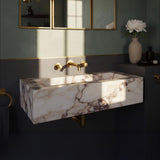 A luxurious Calacatta Amber Viola marble sink, wall-mounted with elegant brass fixtures in a high-end bathroom.