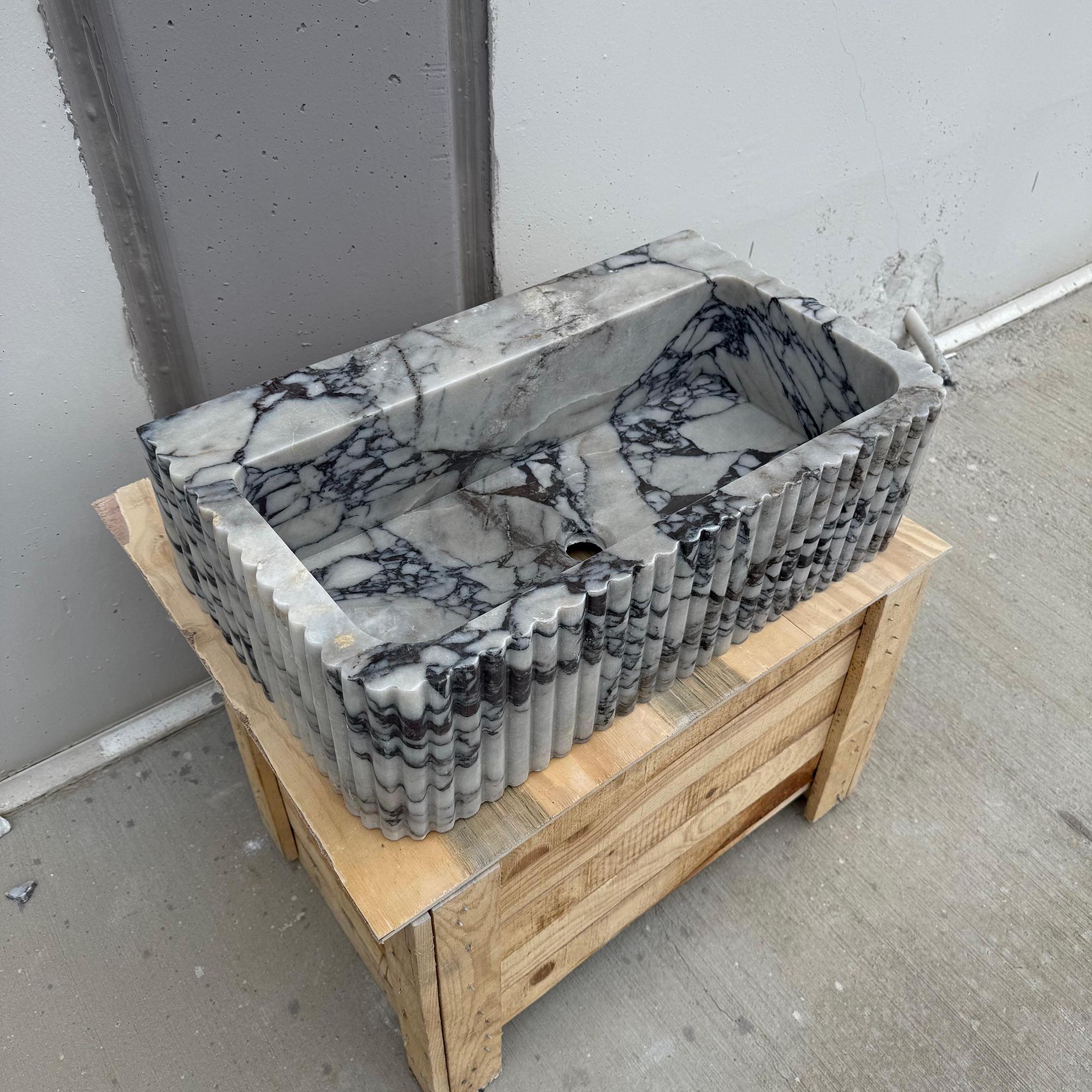 This photo shows a ribbed rectangular vessel sink made from dramatic Calacatta Viola marble.