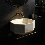 Sculptural white marble basin in octagonal form, paired with luxurious gold bathroom fixtures.