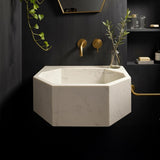 Octagon-shaped Carrara marble sink mounted on a dark luxury bathroom wall with gold fixtures.