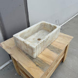 Fluted rectangular Calacatta Gold marble sink on wooden surface.