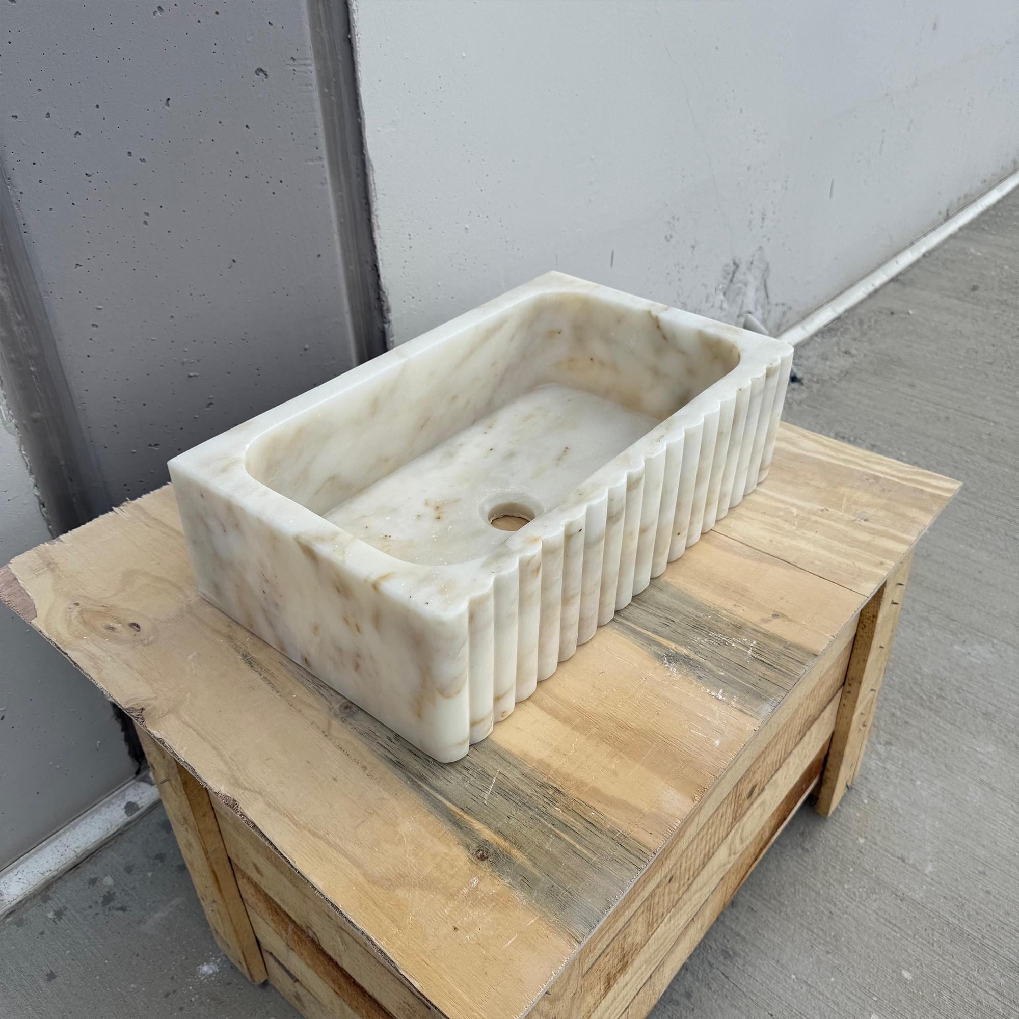 Fluted rectangular Calacatta Gold marble sink on wooden surface.