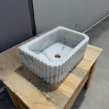 Fluted Carrara marble sink with soft grey veining on wooden surface