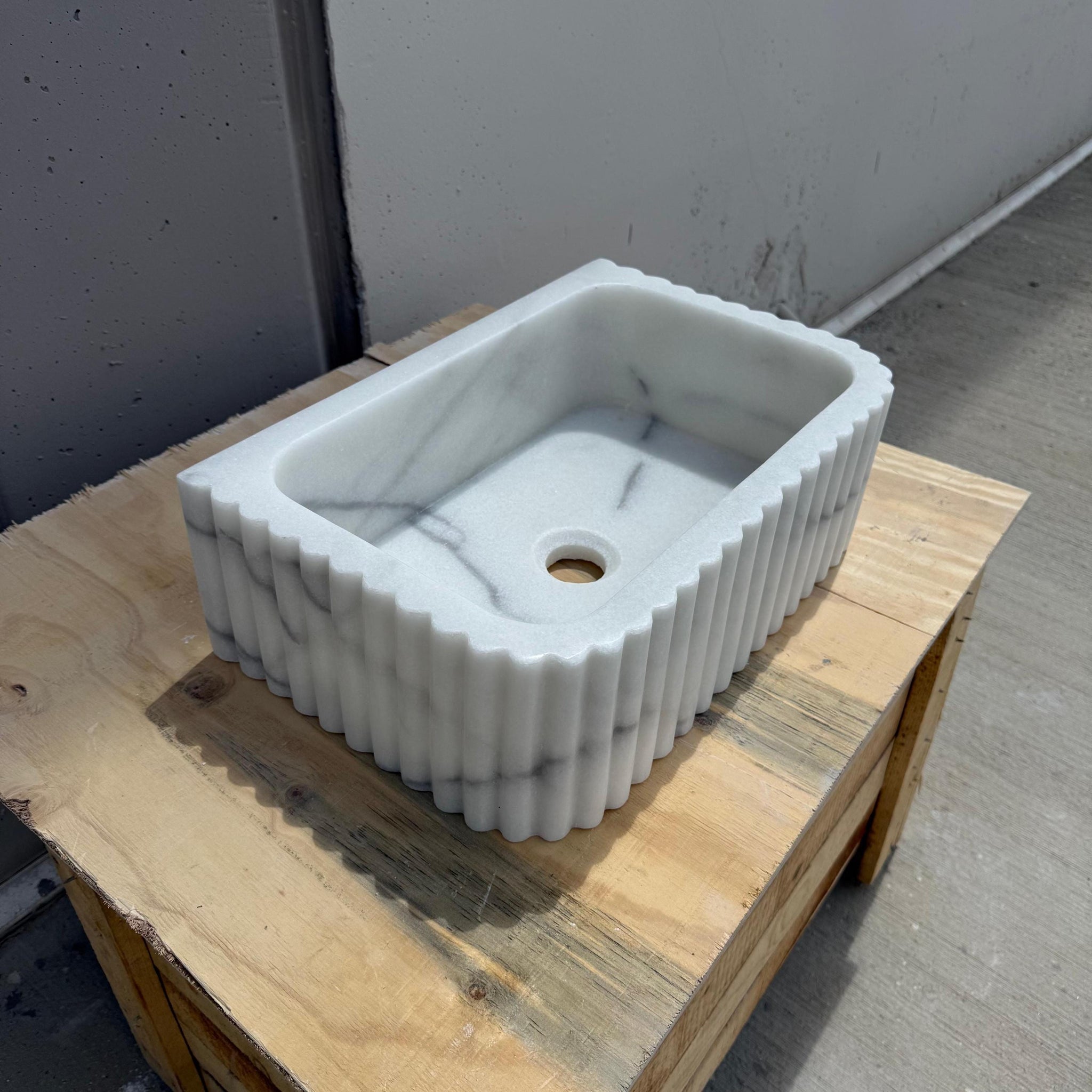 Fluted Carrara marble sink with soft grey veining on wooden surface