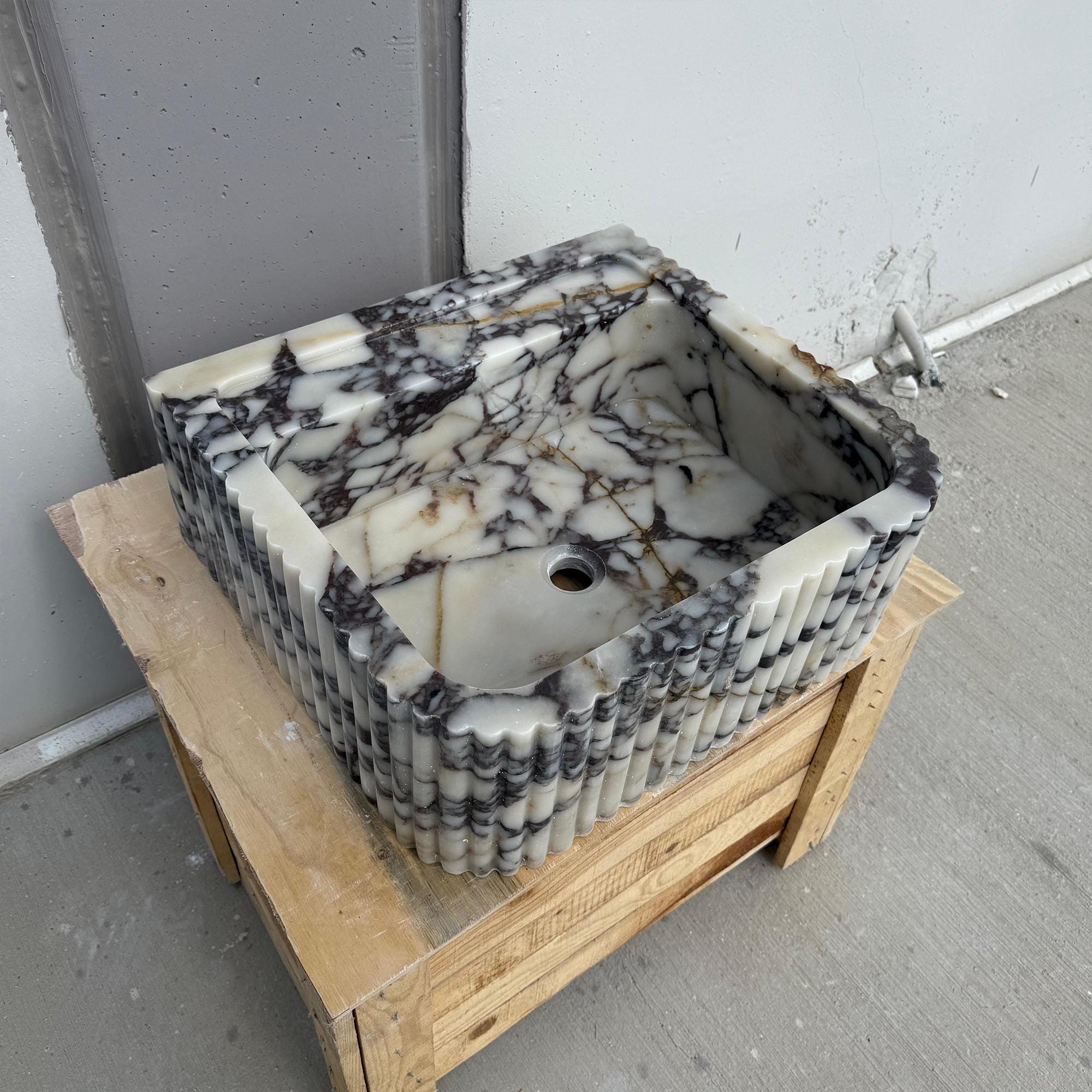 A luxury bathroom basin made of Calacatta Viola marble, featuring a square form with softly fluted exterior detailing.