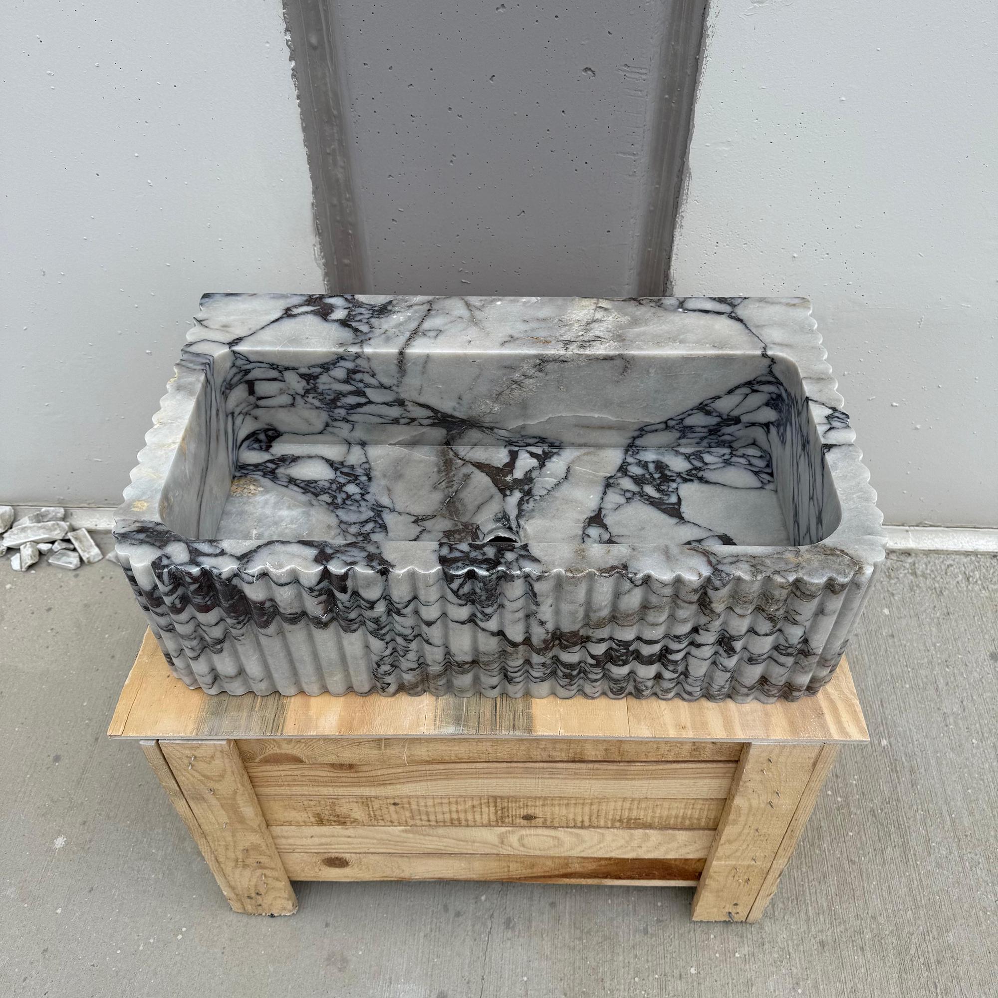 A sculptural rectangular basin crafted from Calacatta Viola marble sits on a wooden crate.