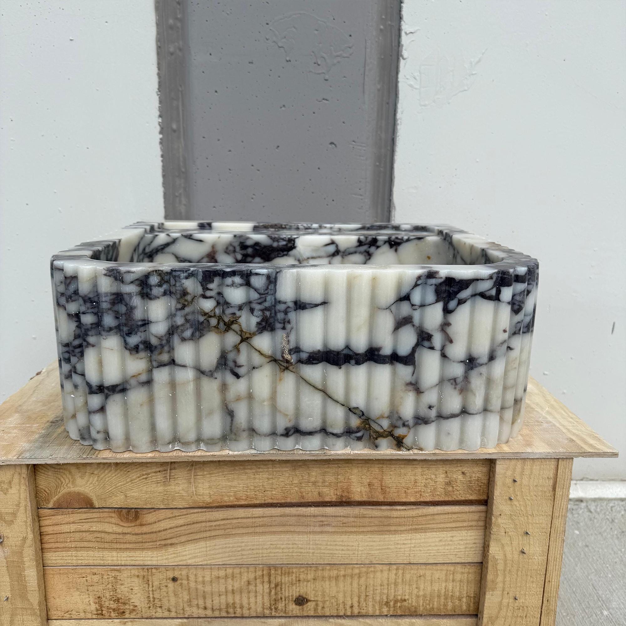 This fluted square sink is crafted from Calacatta Viola marble with dramatic dark veining and a sculpted stone finish.