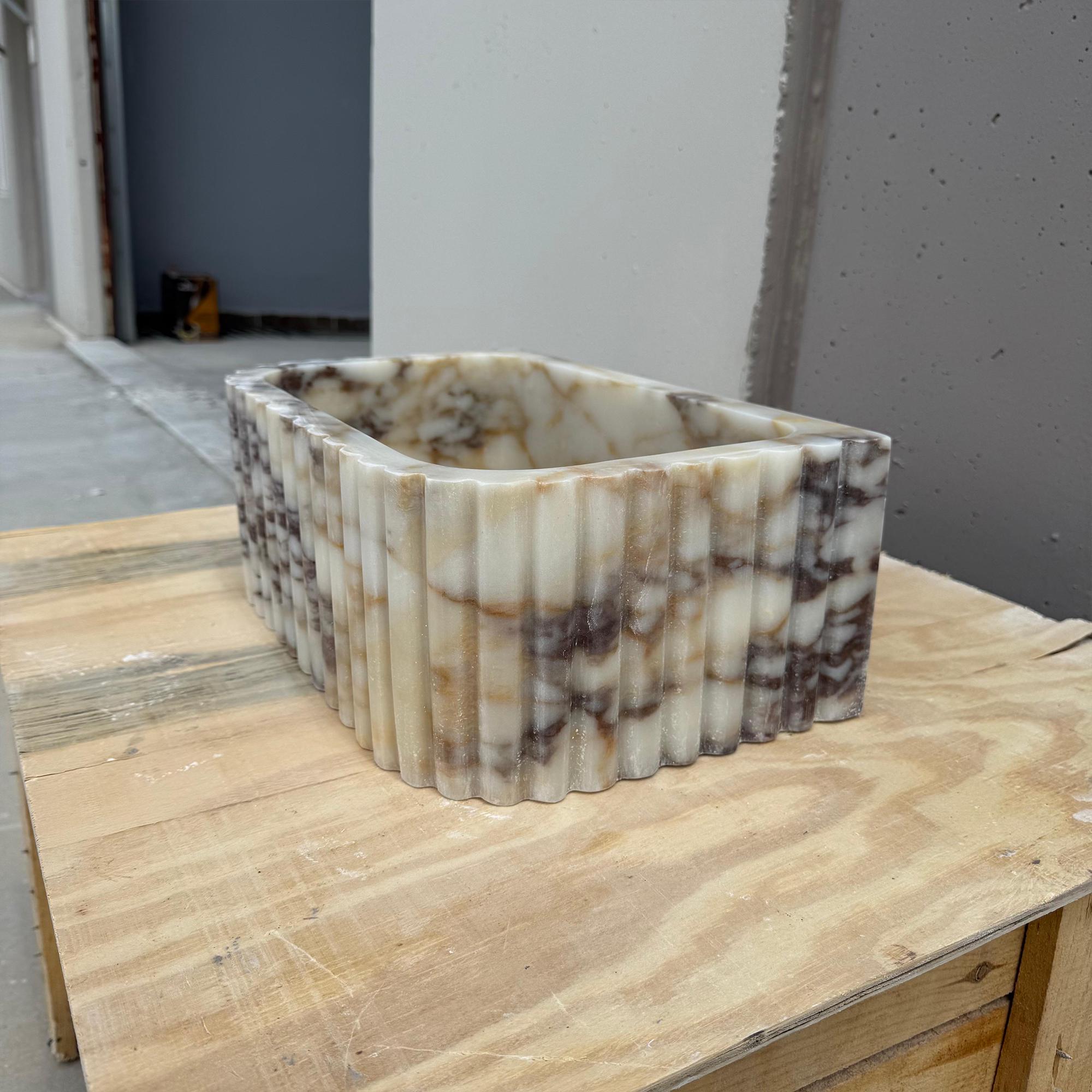 The image highlights the natural veining and soft tones of a fluted marble bathroom sink.