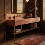 A luxurious wall-mounted pink marble sink with brass fixtures and wood shelving.