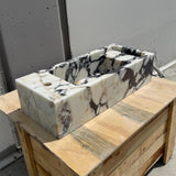A compact rectangular sink made from Calacatta Viola marble with bold veining and a built-in faucet hole.