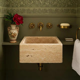 A wall-mounted rectangular travertine sink featured against a deep olive green backdrop with brass fixtures.