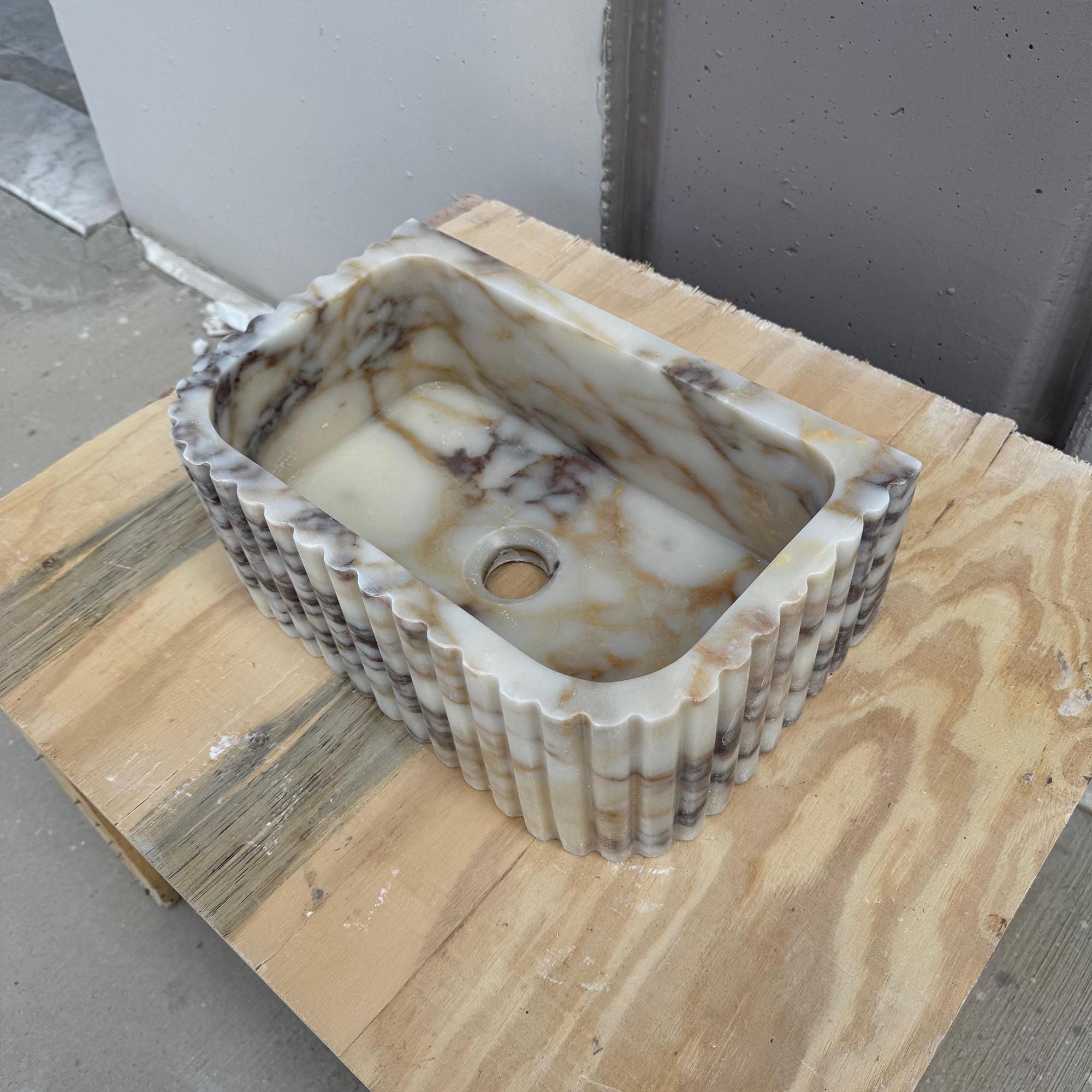 The sink showcases elegant vertical grooves carved into authentic Carrara marble.